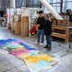 A student looks at a large-scale painting on the floor with Professor Linda Geary.