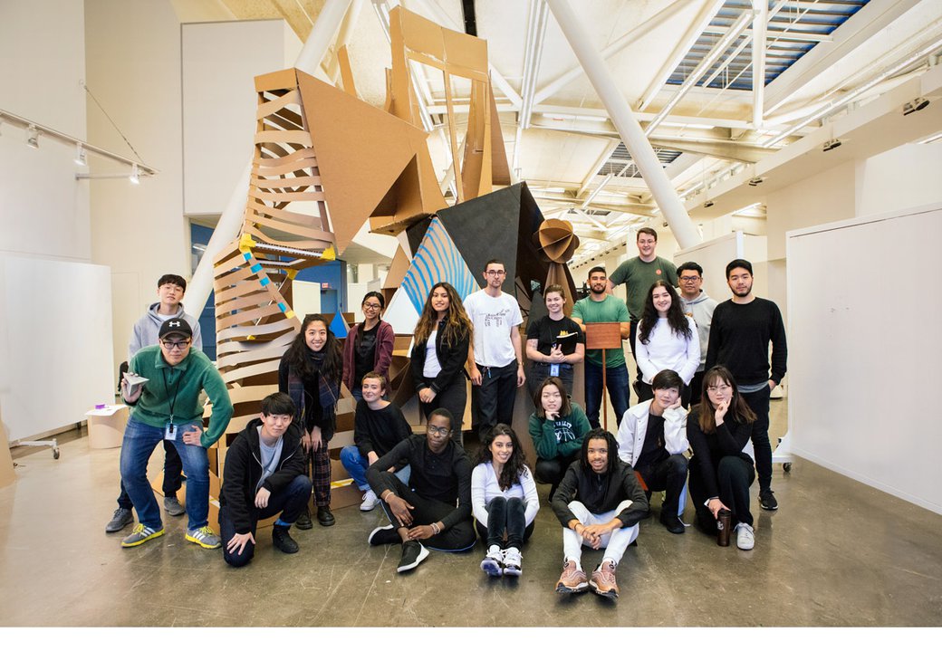 A group of architecture students poses in front of a large cardboard structure.