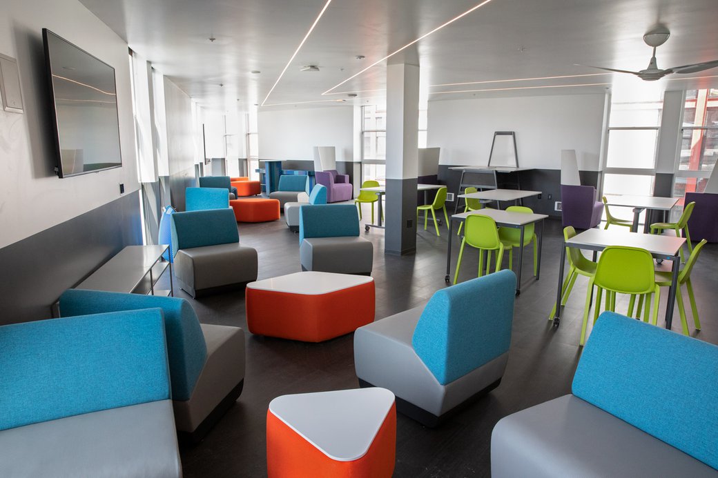 Common area room with orange stools, blue backed seats, and orange chairs.