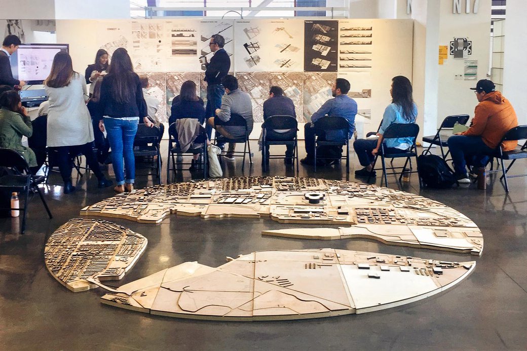 A group of people sit in front of a board of artwork, behind them is a large, wooden puzzle.