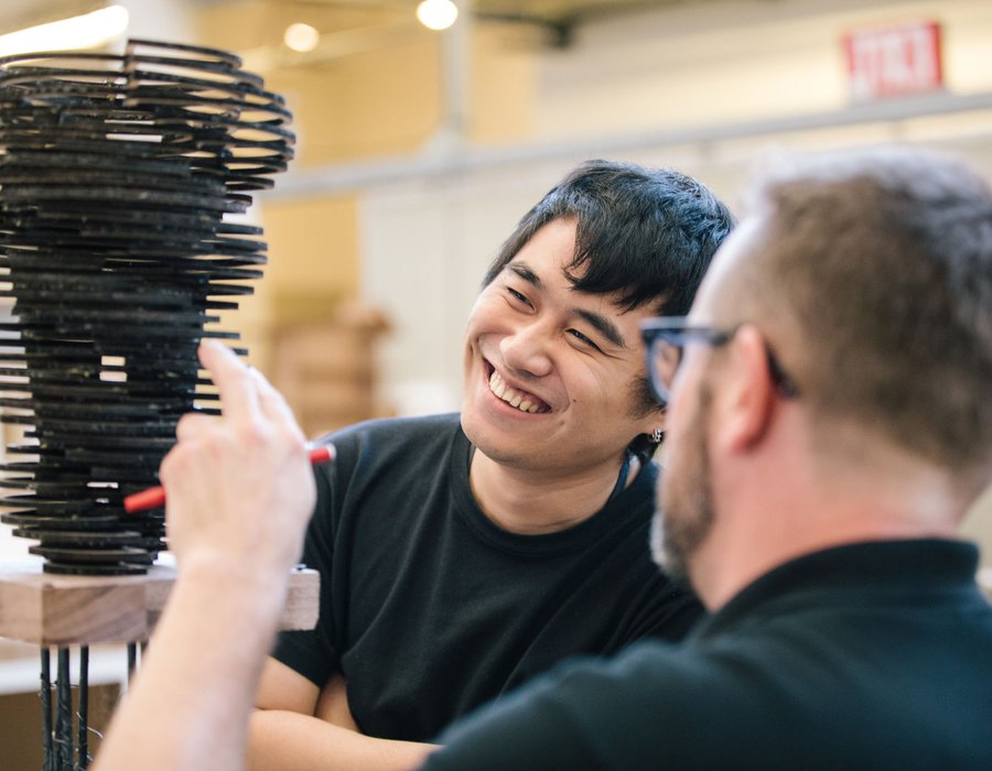 An architecture student smiles as a professor points at their model.
