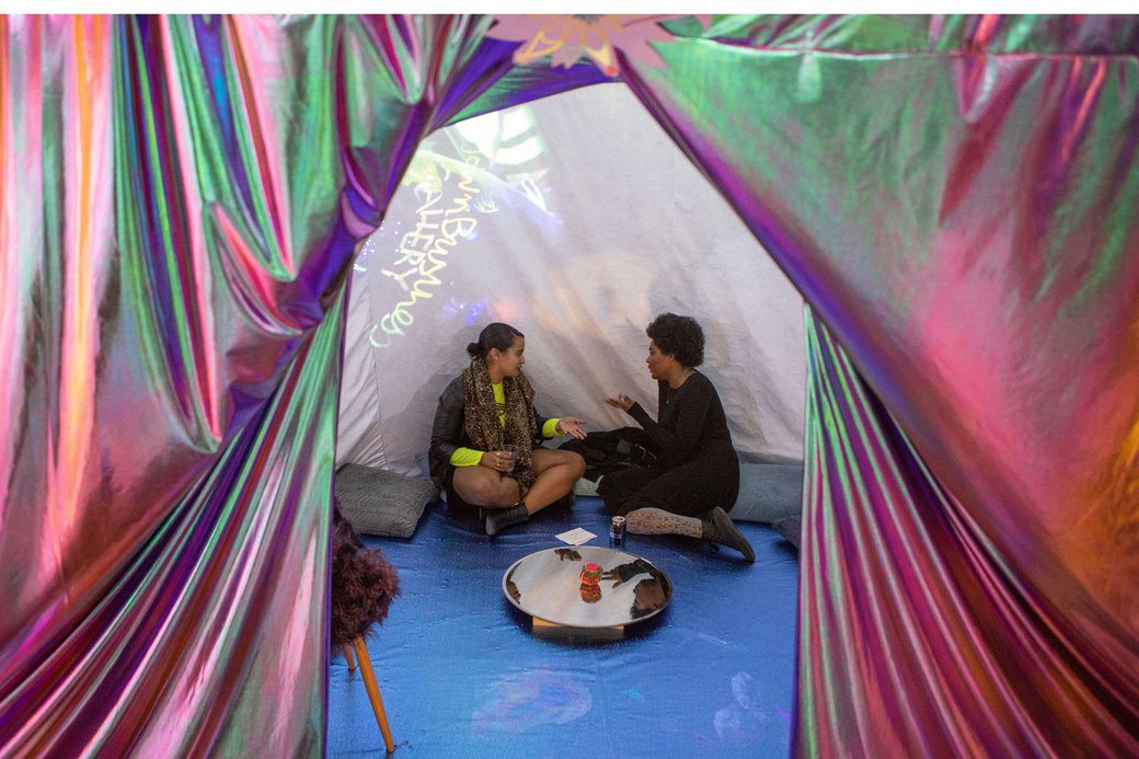 Two students sit inside of a tent installation during the MFA grad show.