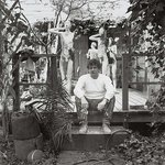 Manuel Neri sits in front of his sculptures in a black and white photograph