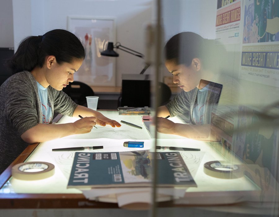 Illustration student drafting on a light table in her studio