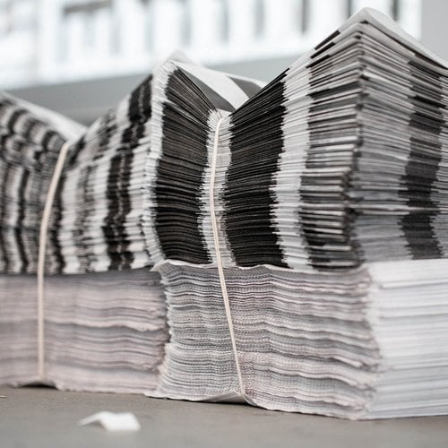 Stacks of printed newsprint compose the layered background of the on-site installation.