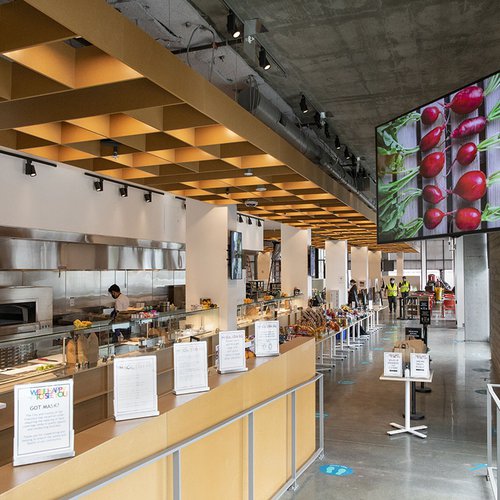 Interior view of Makers Cafe, an open kitchen and grill on the left and TV screen with a photo of beets above on the right.