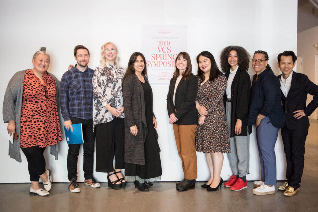 A group of graduate students pose next to a sign that says, "2019 VCS Spring Symposium."