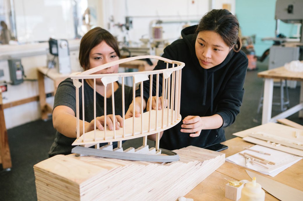 Two students assist each other in adjusting an architectural model.