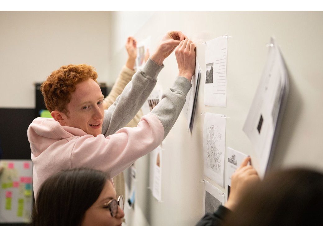 student pinning up their work in the "border phenomena" class