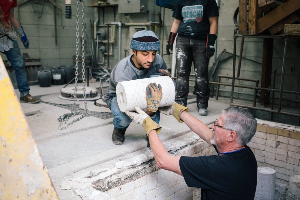 Student and faculty lift sculpture molds out of the kiln in the foundry.