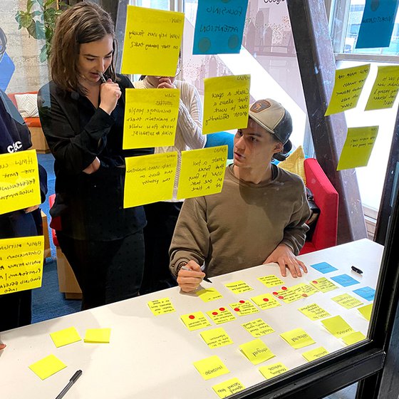 Eva Xu, Olive Brown, and Ryan Koble viewing yellow post-it notes on a glass wall at Google.