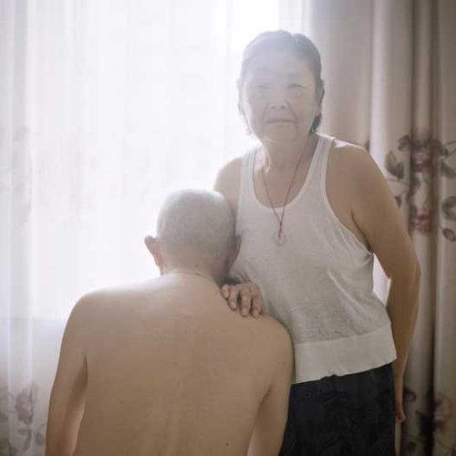 Old man leans against an old woman in a moment of domestic intimacy.