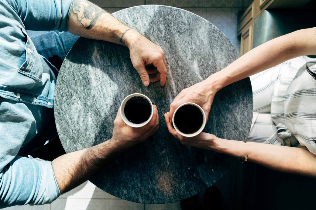 Two coffee-filled mugs, each held by a hand.