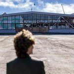 Architect Jeanne Gang stands with her back to the camera as she visits the construction site of the new “Double Ground” expansion project for California College of the Arts in San Francisco. She looks toward the current building across a flat, dirt lot where the new campus will be built.