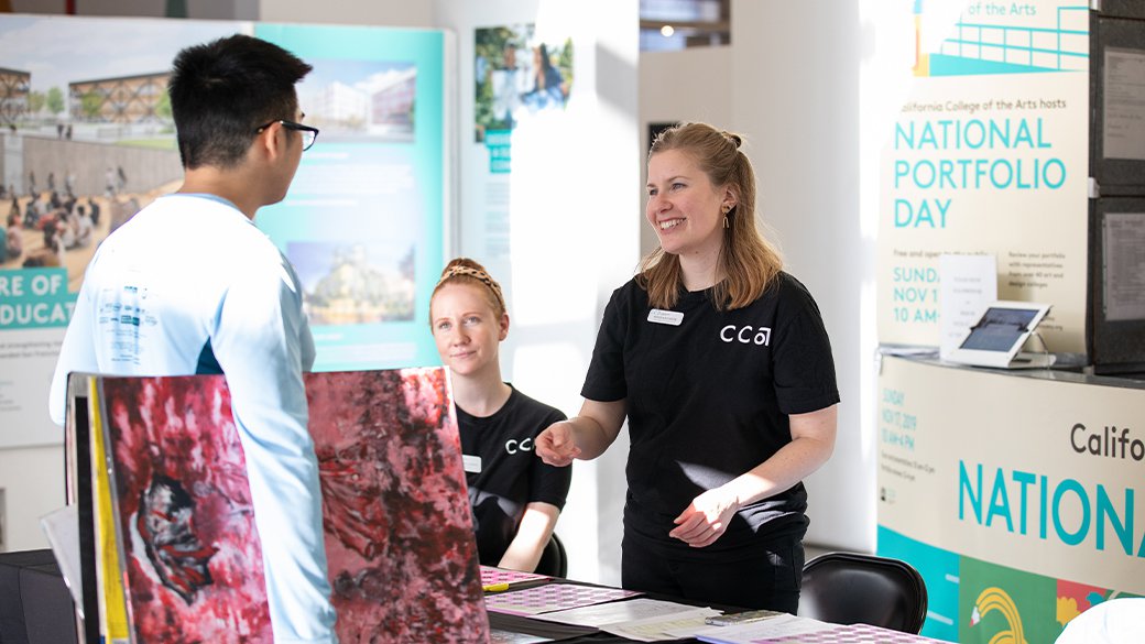A student holding a large painting shakes hands with two CCA admissions counselors at the 2019 National Portfolio Day.